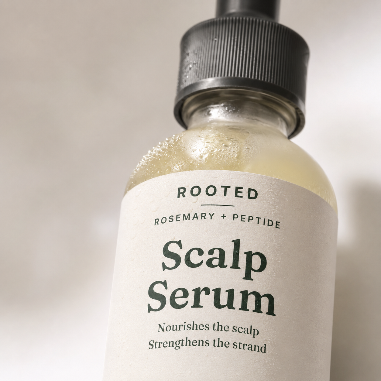 Close-up of the ROOTED Scalp Serum label with water droplets on the glass